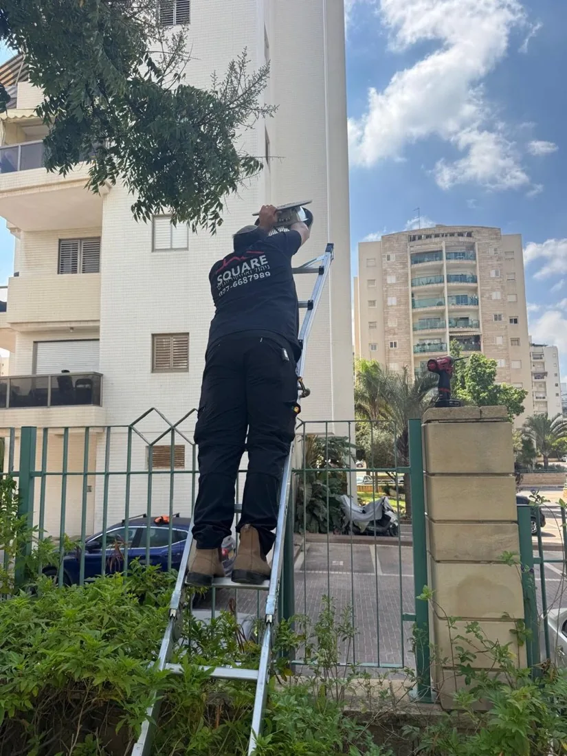 עובד SQUARE על סולם מטפל בתאורת החוץ של הבניין