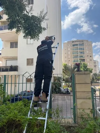 עובד SQUARE על סולם מטפל בתאורת החוץ של הבניין