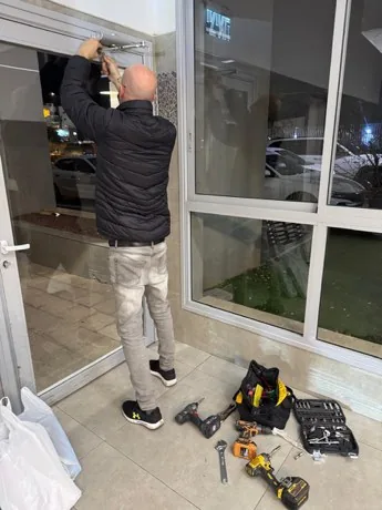 עובד מטפל בדלת הכניסה מזכוכית של הבניין, עם ארגז כלים פתוח